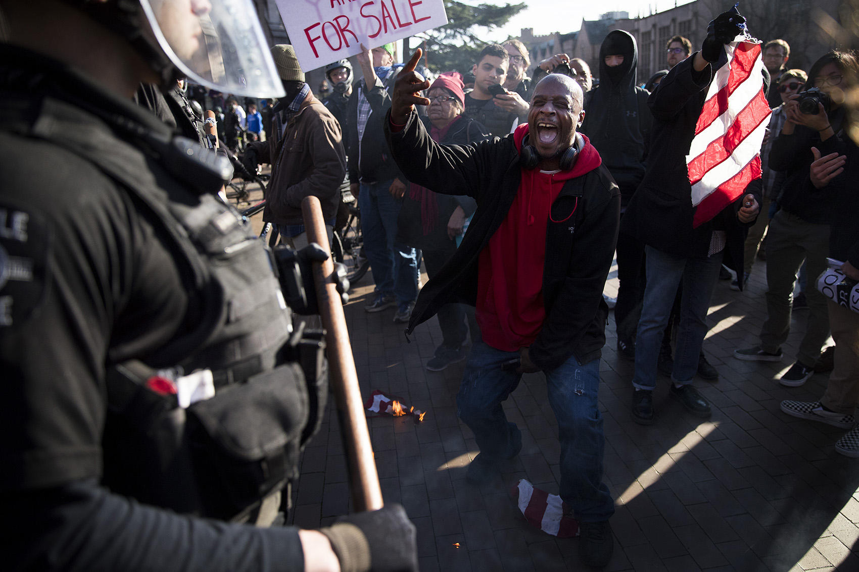 Jamal X, center, yells at police officers after lighting a portion of an American Flag on fire while protesting outside of a College Republicans rally on Saturday, Feb. 10, 2018, at Red Square on the University of Washington campus in Seattle. CREDIT: MEGAN FARMER