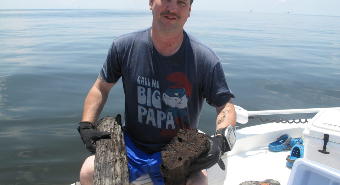 Ben Raines, an environmental reporter for AL.com, holds pieces of wood he collected from a cypress forest discovered in the depths of the Gulf of Mexico. A scientist says having an intact forest from the ice age is rare. CREDIT: DEBBIE ELLIOTT/ NPR