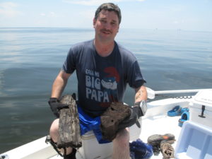 Ben Raines, an environmental reporter for AL.com, holds pieces of wood he collected from a cypress forest discovered in the depths of the Gulf of Mexico. A scientist says having an intact forest from the ice age is rare. CREDIT: DEBBIE ELLIOTT/ NPR