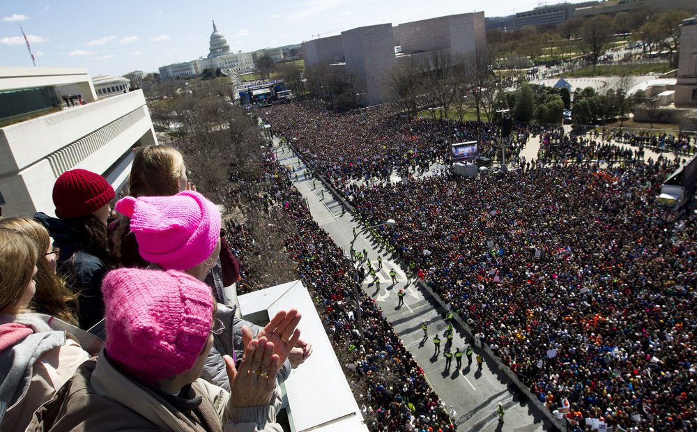 People on the balcony at the Newseum cheer the protesters on Pennsylvania Avenue as they look toward the stage near the Capitol in Washington.