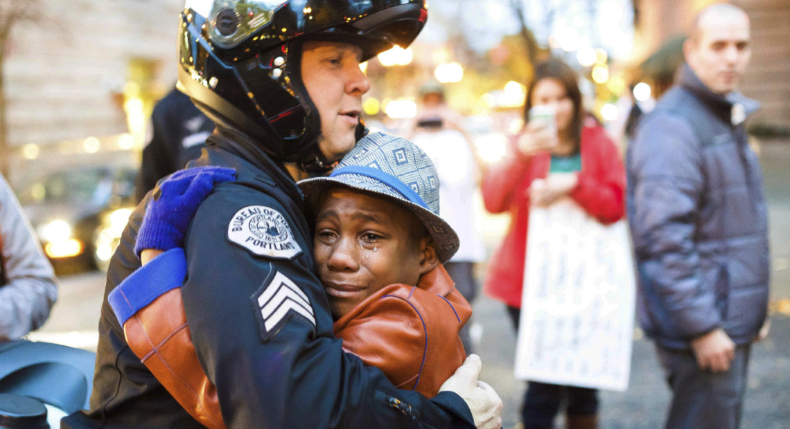 A photo of 12-year-old Devonte Hart went viral in 2014 as he hugged a police officer during a protest against police violence. Less than four years later, the now-15-year-old is feared dead alongside his entire family in a car crash. CREDIT: JOHNNY HUU NGUYEN/AP