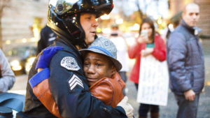A photo of 12-year-old Devonte Hart went viral in 2014 as he hugged a police officer during a protest against police violence. Less than four years later, the now-15-year-old is feared dead alongside his entire family in a car crash. CREDIT: JOHNNY HUU NGUYEN/AP