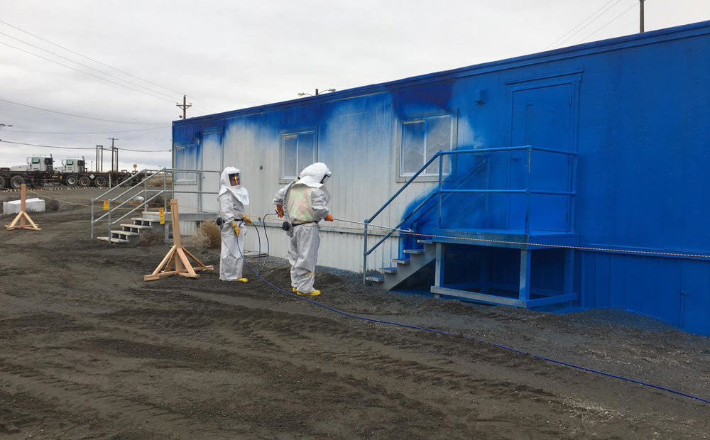 Crews in white suits applying a coat of fixative, or a paint-like substance to prevent contamination on the wall of an mobile office trailer at the PFP.