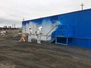 Crews in white suits applying a coat of fixative, or a paint-like substance to prevent contamination on the wall of an mobile office trailer at the PFP.