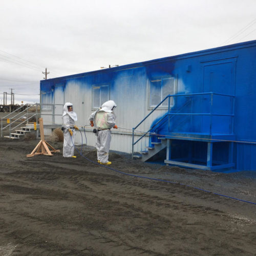 Crews in white suits applying a coat of fixative, or a paint-like substance to prevent contamination on the wall of an mobile office trailer at the PFP.