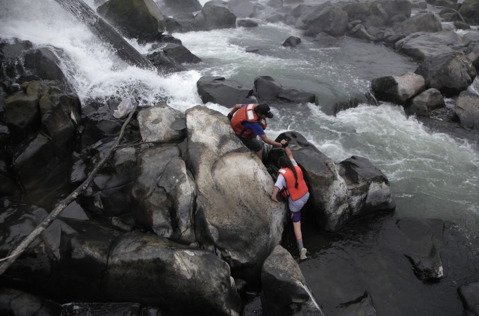 The upcoming generation of lamprey harvesters. Henry Begay helps his younger sister, Jackie, scale the slippery rocks at the base of Willamette Falls. CREDIT: IAN MCCLUSKEY