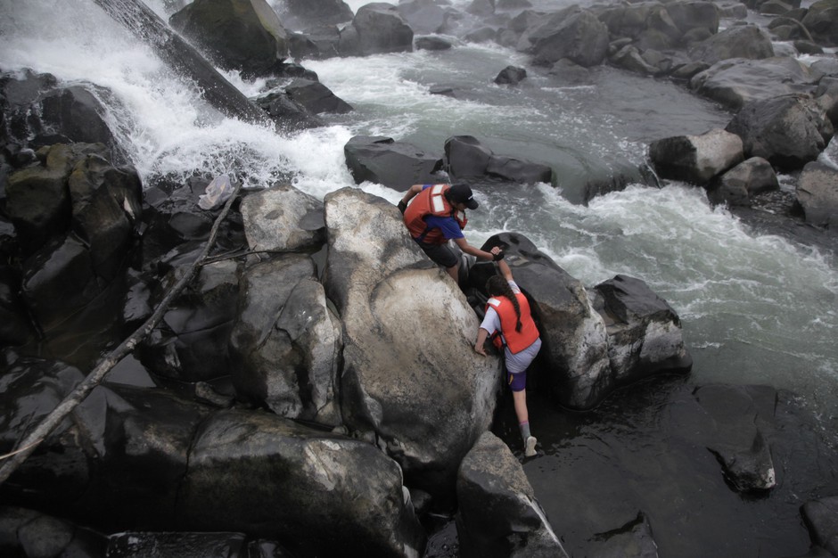 The upcoming generation of lamprey harvesters. Henry Begay helps his younger sister, Jackie, scale the slippery rocks at the base of Willamette Falls. CREDIT: IAN MCCLUSKEY