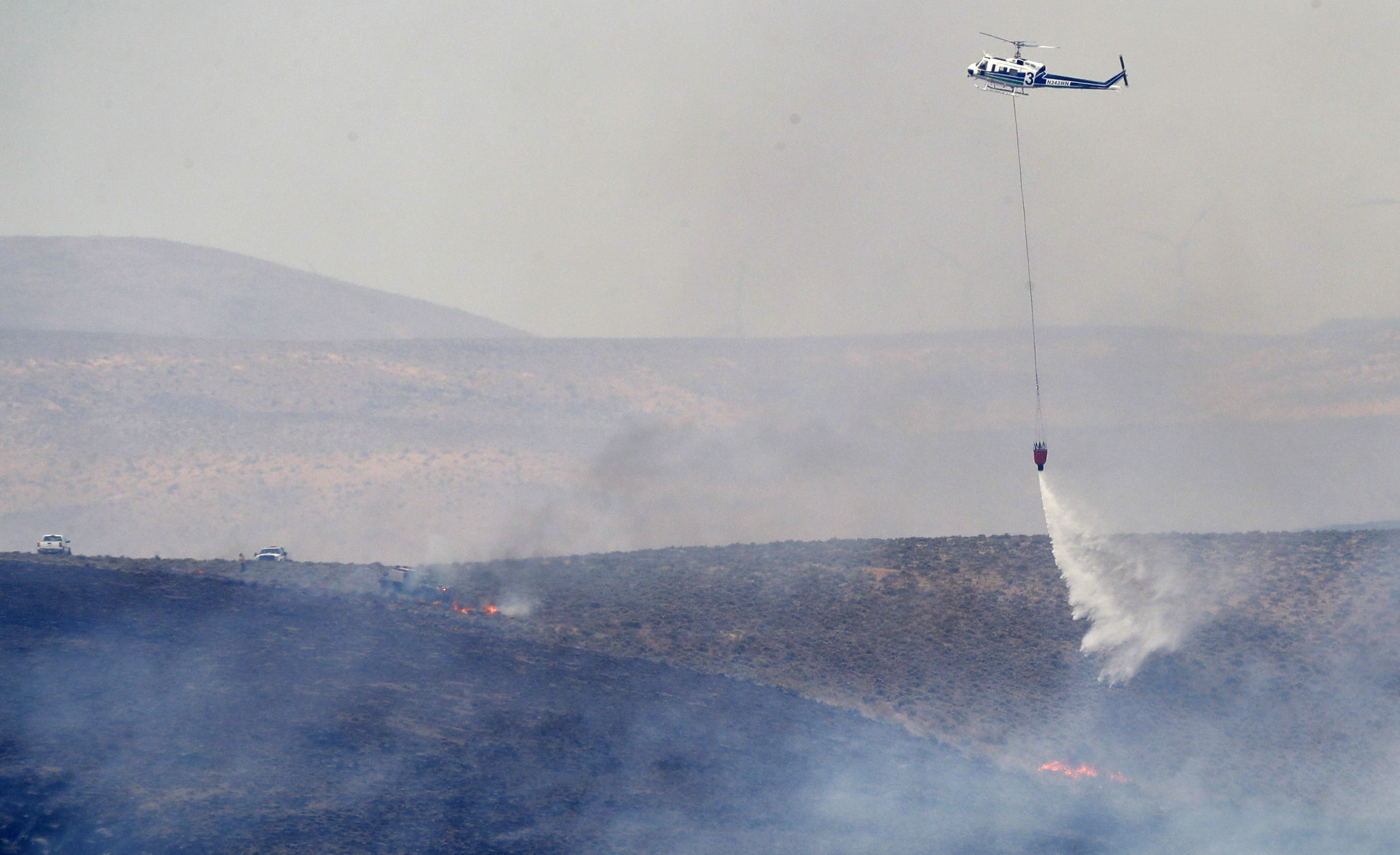 A helicopter uses a bucket to drop water on the Milepost 22 wildfire, Thursday, June 21, 2018, near Vantage, Wash. CREDIT: AP PHOTO/TED S. WARREN