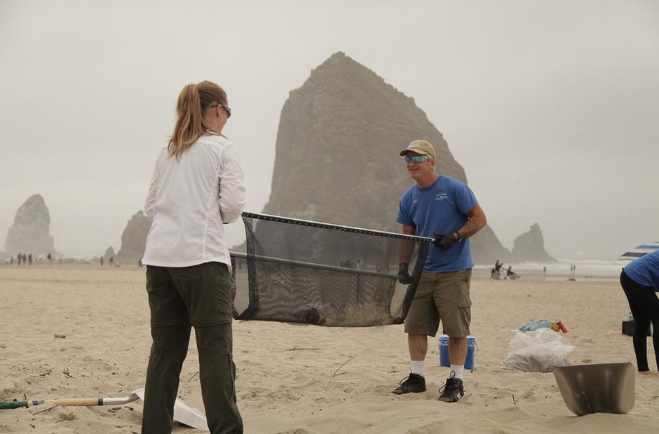 Valerie Schockelt (left) and Marc Ward use a microplastics filtration device to filter sand on Cannon Beach with iconic Haystack Rock in the background. CREDIT: JOSEPH WINTERS, OPB/EARTHFIX