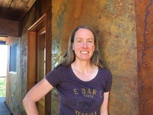 Amy Snover, director of the Climate Impacts Group at the University of Washington, stands outside her family’s cabin in Pine Forest. She replaced the wood siding on the house with metal siding to improve fire resistance and participated in community tree-thinning efforts. CREDIT: ASHLEY AHEARN