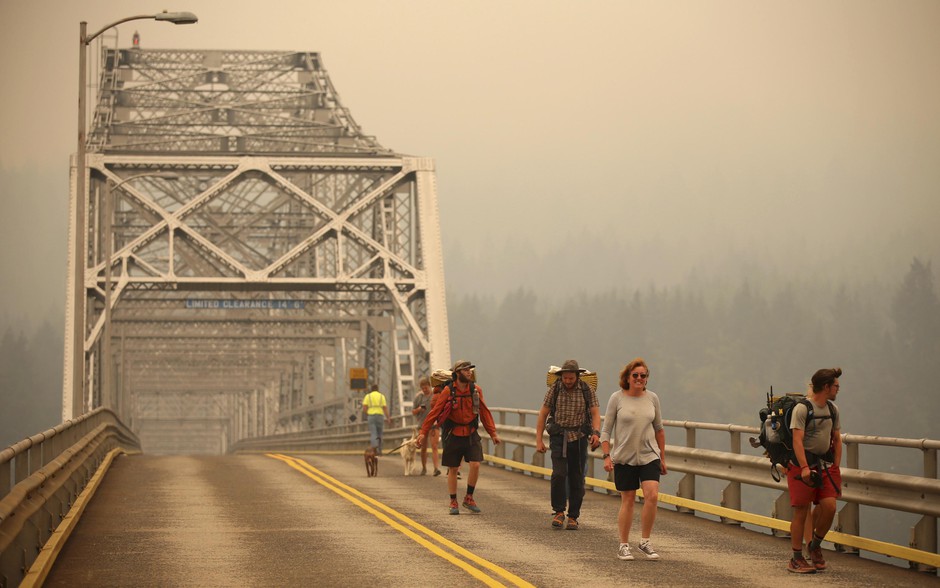 Pedestrians walk off the Bridge of the Gods, which spans the Columbia River between Washington and Oregon, as smoke from the Eagle Creek Fire obscures the Oregon hills in the background near Stevenson, Washington, Wednesday, Sept. 6, 2017. CREDIT: RANDY L. RASMUSSUN/AP