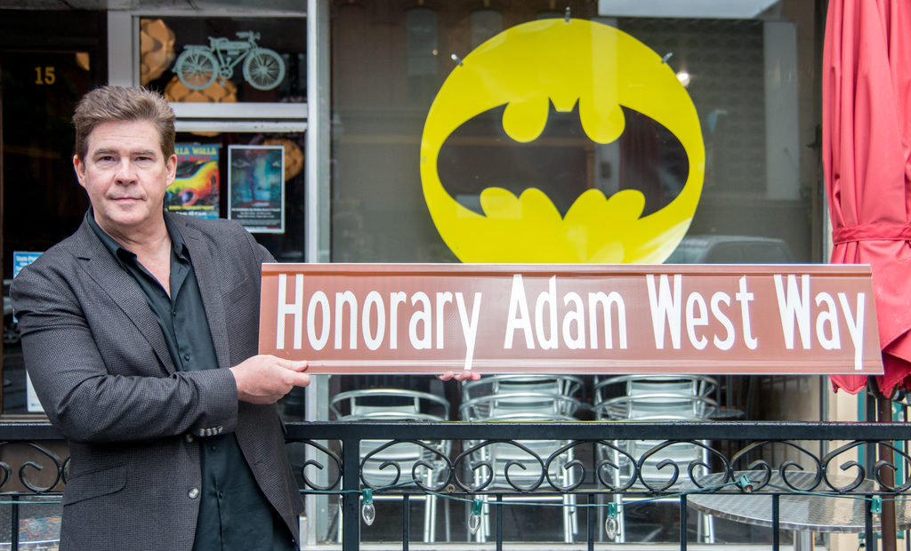 Actor who worked with Adam West holding a sign reading Honorary Adam West Way.