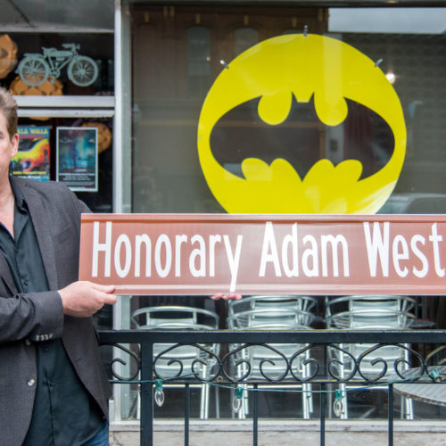 Actor who worked with Adam West holding a sign reading Honorary Adam West Way.
