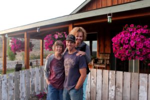 Maura Hammack, left, Albert Rollins and Kelli Jo Hammack stand in front of their house outside Madras, Oregon. John Hammack, the patriarch of the family, was killed in 2013 by a burning, falling tree. CREDIT: TONY SCHICK