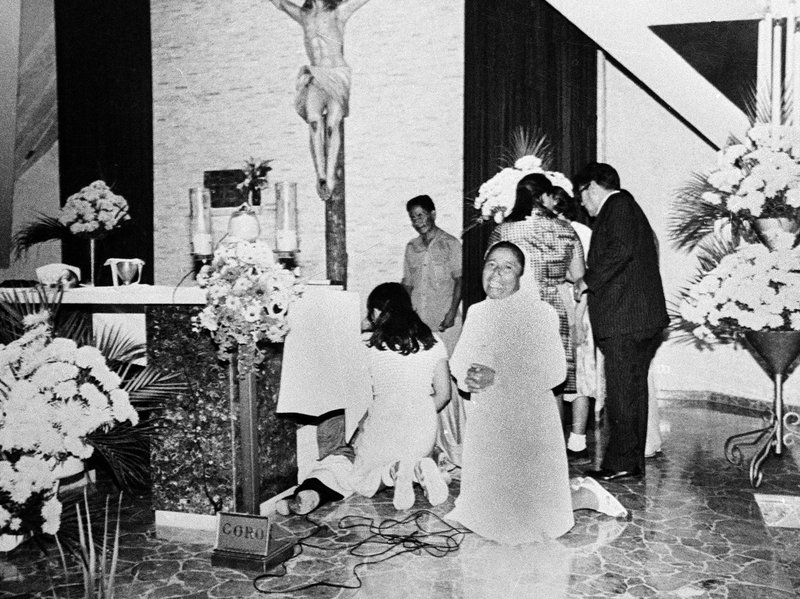 A nun clasps her hands in prayer as others gather around Romero after he was shot at the altar while celebrating Mass in 1980. CREDIT: AP