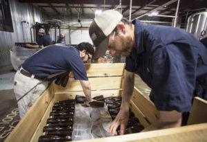 Allagash employees Salim Raal, left, and Brendan McKay stack bottles of Golden Brett, a limited release beer fermented with a house strain of Brettanomyces yeast. The Maine brewery recently installed solar panels as part of its sustainability initiatives. CREDIT: DEREK DAVIS