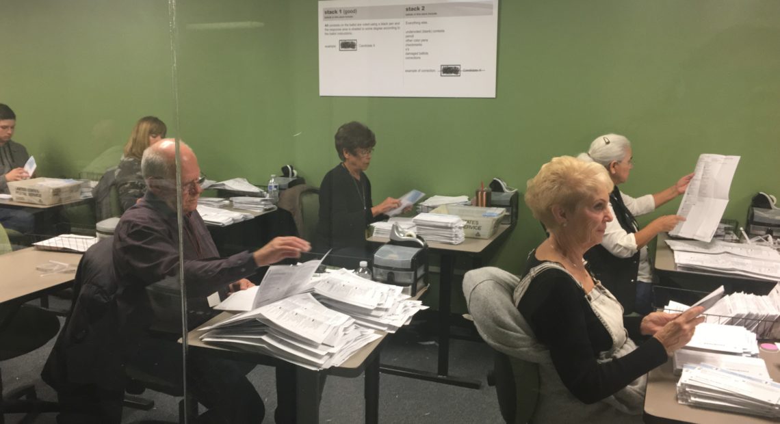 Workers in the Yakima County Elections Office work to open ballots and verify information. Their work is done within public view behind a glass wall, for anyone to monitor. CREDIT: ESMY JIMENEZ/NWPB