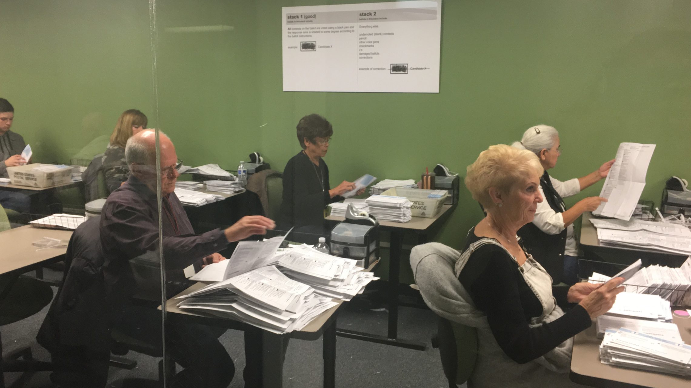 Workers in the Yakima County Elections Office work to open ballots and verify information. Their work is done within public view behind a glass wall, for anyone to monitor. CREDIT: ESMY JIMENEZ/NWPB