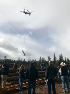 People watch on as a helicopter lifts logs into the air. CREDIT: COURTNEY FLATT