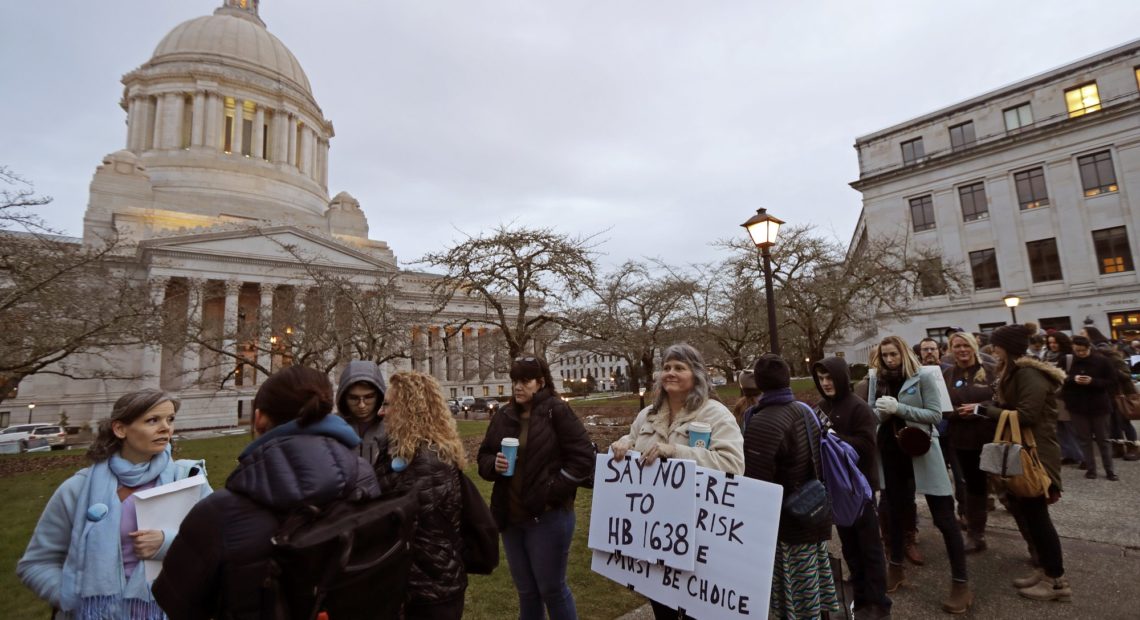 Kebby Johnson, center, of Spokane, Wash., holds a sign that reads "Say No to HB 1638," as she waits in line, Friday, Feb. 8, 2019, to attend a public hearing before the House Health Care & Wellness Committee at the Capitol in Olympia, Wash. Amid a measles outbreak that has sickened people in Washington state and Oregon, lawmakers heard public testimony Friday on a bill that would remove parents' ability to claim a philosophical exemption to opt their school-age children out of the combined measles, mumps and rubella vaccine. CREDIT: TED S. WARREN/AP