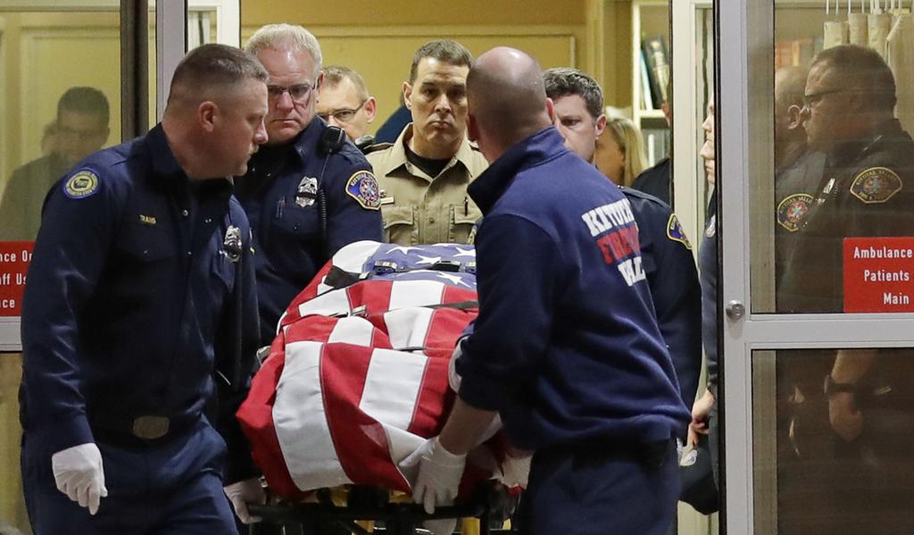 The body of a Kittitas County Sheriff's deputy is draped with a U.S. flag as it is carried out of Kittitas Valley Healthcare Hospital in the early morning hours of Wednesday, March 20, 2019, in Ellensburg, Wash., as seen through a large circular entry window. A sheriff's deputy was killed and a police officer was injured after an exchange of gunfire during an attempted traffic stop. CREDIT: TED S. WARREN/AP