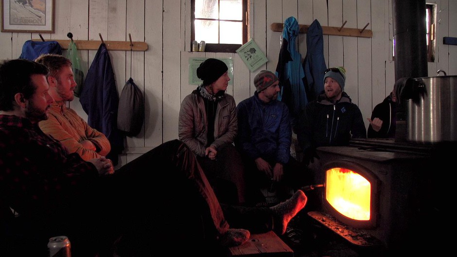 Backcountry skiers staying warm by the woodstove inside the Tilly Jane A-frame. CREDIT: GREG DAVIS/OPB