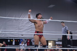 Wrestler, Simon Grimm, in red shorts, poses in the ring. 