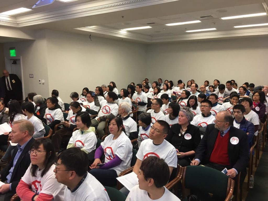 Opponents of I-1000 in white t-shirts packed a hearing room in Olympia. CREDIT AUSTIN JENKINS/N3