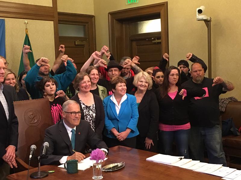 Vape shop owners give the thumbs down sign as Gov. Jay Inslee poses for a photo after signing into law a new tax on vaping liquids. CREDIT: AUSTIN JENKINS/N3