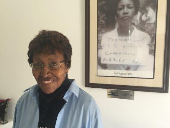 Civil rights "foot soldier" Theresa Burroughs in 2016, in front of a photo of the day she was arrested in 1965. Burroughs has died at age 89. Debbie Elliott/NPR