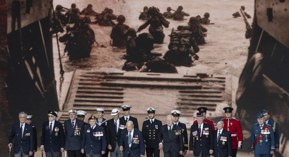 Veterans stand in front of a 1944 image of their comrades wading onto the beaches of France during D-Day commemorations in Portsmouth, England. Leaders of 16 countries involved in World War II joined Queen Elizabeth II at the ceremony on Wednesday. Dan Kitwood/Getty Images