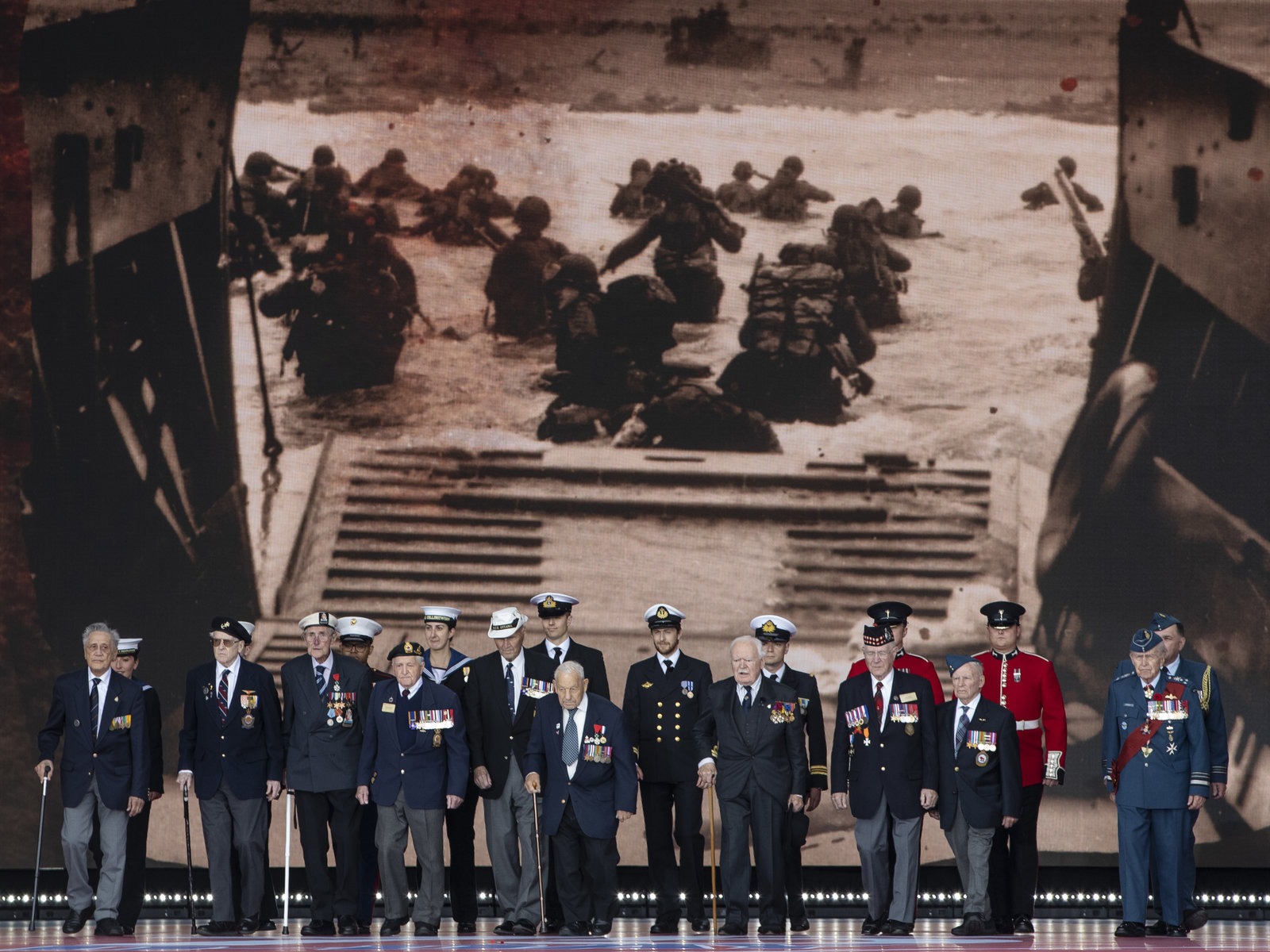 Veterans stand in front of a 1944 image of their comrades wading onto the beaches of France during D-Day commemorations in Portsmouth, England. Leaders of 16 countries involved in World War II joined Queen Elizabeth II at the ceremony on Wednesday. Dan Kitwood/Getty Images
