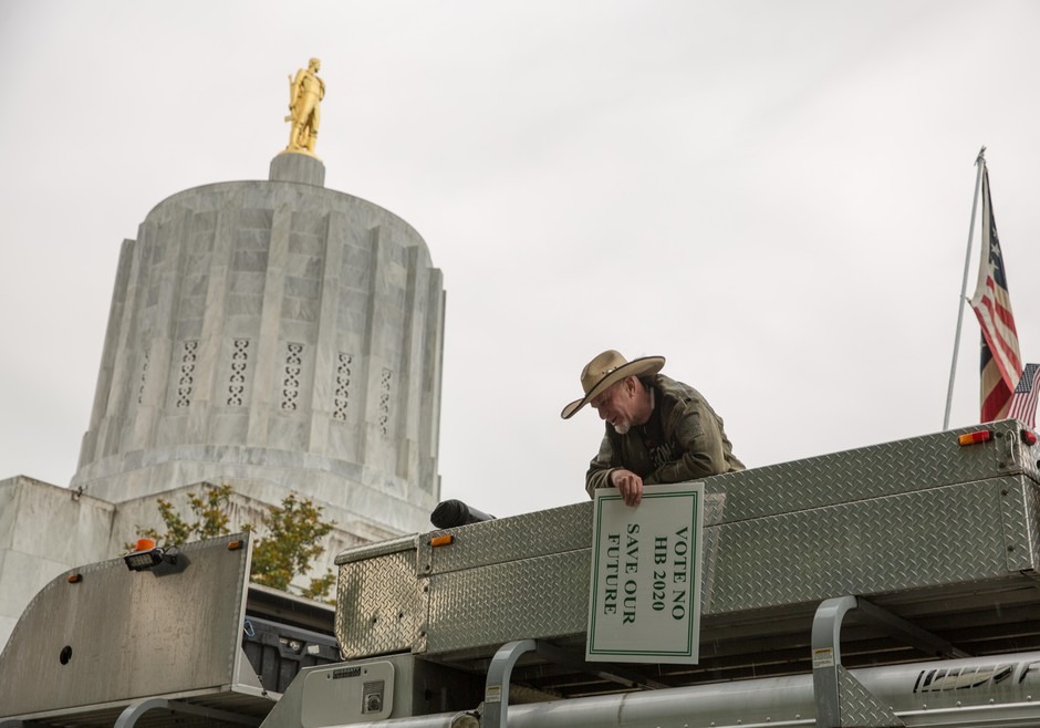 A man holding a sign in opposition to Oregon House Bill 2020 talks to fellow rallygoers from the roof of a truck at an event on the Oregon Capitol steps in Salem, Ore., on Thursday, June 27, 2019. CREDIT: Bryan M. Vance/OPB