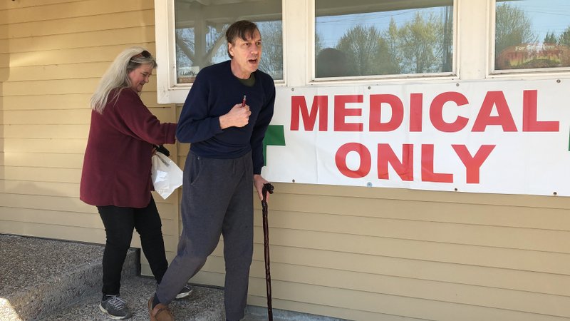 Scott Donnelly, assisted by his wife and licensed caregiver, Vicki Poppen, leaves Western Oregon Dispensary in Sherwood, Ore., after buying medical marijuana to treat muscle spasms caused by his multiple sclerosis. Donnelly visits the medical-only dispensary once a week and relies on it for the cannabis that eases his tremors long enough that he can fall asleep. The dispensary is one of two medical-only shops left in Oregon. CREDIT: GILLIAN FLACCUS/AP