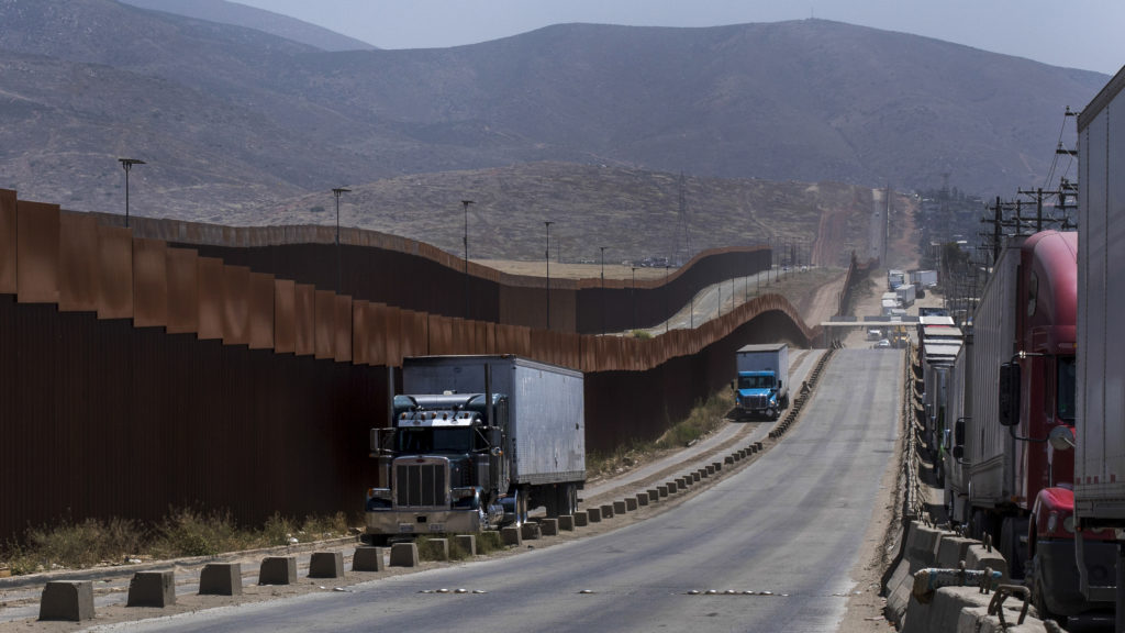 Trucks pass along a border wall as they get into position to cross into the United States at the border in Tijuana, Mexico, on Friday. Companies had been rushing to ship as many goods as possible out of Mexico to get ahead of possible tariffs threatened by President Trump. Hans-Maximo Musielik/APv