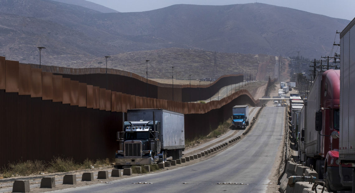 Trucks pass along a border wall as they get into position to cross into the United States at the border in Tijuana, Mexico, on Friday. Companies had been rushing to ship as many goods as possible out of Mexico to get ahead of possible tariffs threatened by President Trump. Hans-Maximo Musielik/APv