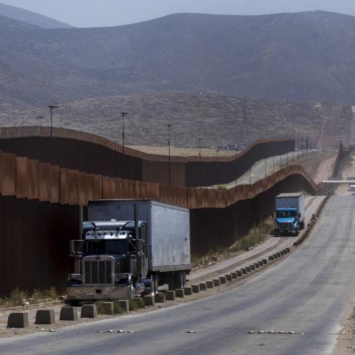 Trucks pass along a border wall as they get into position to cross into the United States at the border in Tijuana, Mexico, on Friday. Companies had been rushing to ship as many goods as possible out of Mexico to get ahead of possible tariffs threatened by President Trump. Hans-Maximo Musielik/APv