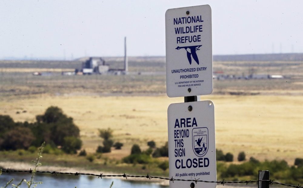 a sign designates a boundary of the Hanford Reach National Monument as the world's first large scale nuclear reactor, the B Reactor, is seen in the background. CREDIT: ELAINE THOMPSON/AP