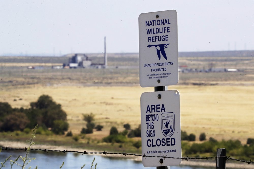 a sign designates a boundary of the Hanford Reach National Monument as the world's first large scale nuclear reactor, the B Reactor, is seen in the background. CREDIT: ELAINE THOMPSON/AP