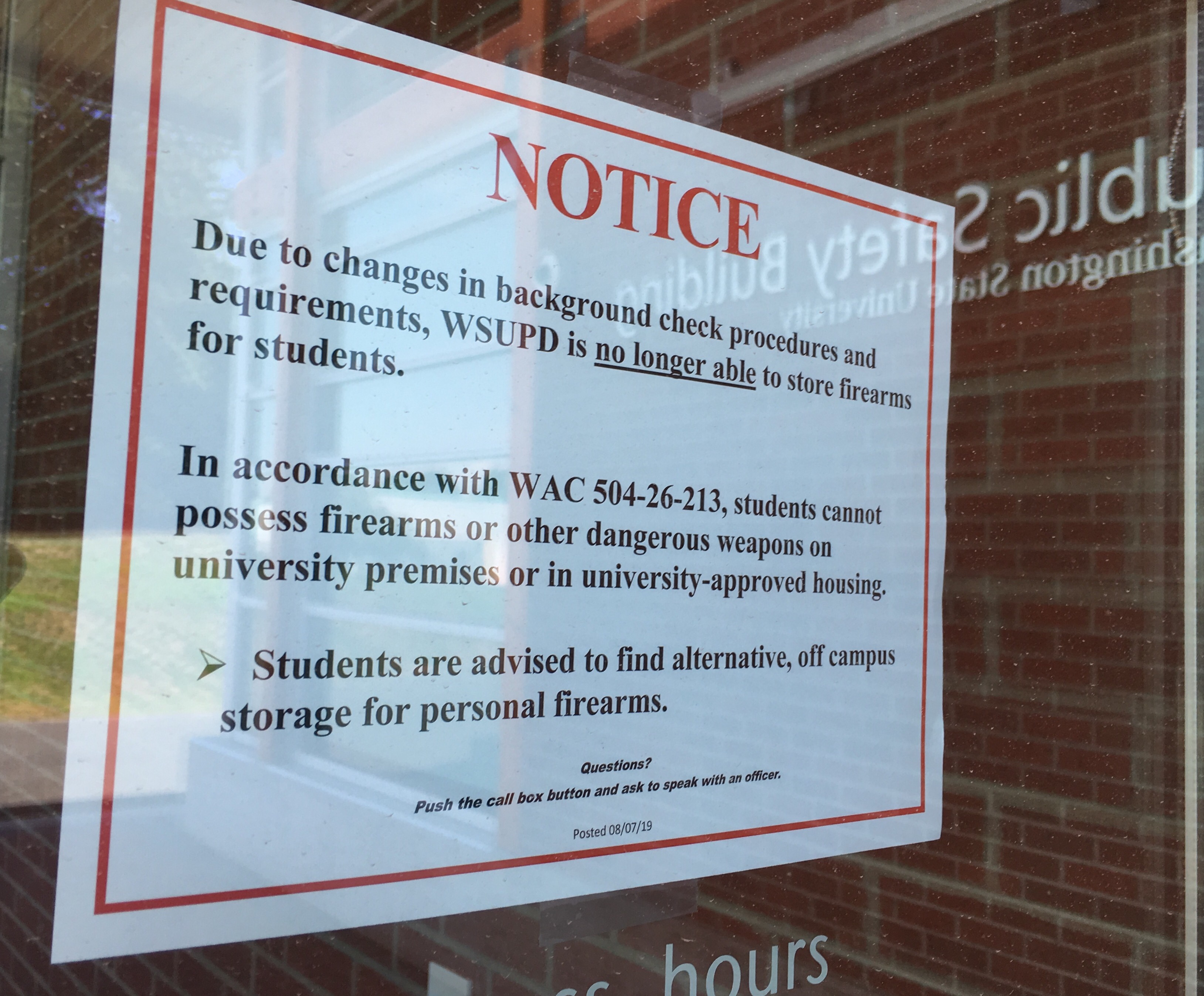 Reflecting on the glass door of the WSU Public Safety Building, a sign on the door announces the gun storage policy change Aug. 14, 2019. CREDIT: SCOTT LEADINGHAM/NWPB