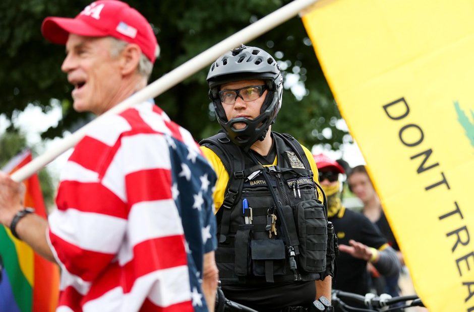 Portland police watch as a Proud Boys rally continues under the Hawthorne Bridge in Portland, Ore., Saturday, Aug. 17, 2019. The Proud Boys espouse white supremacist ideology and have been designated a hate group by the Southern Poverty Law Center. CREDIT: Bradley W. Parks/OPB