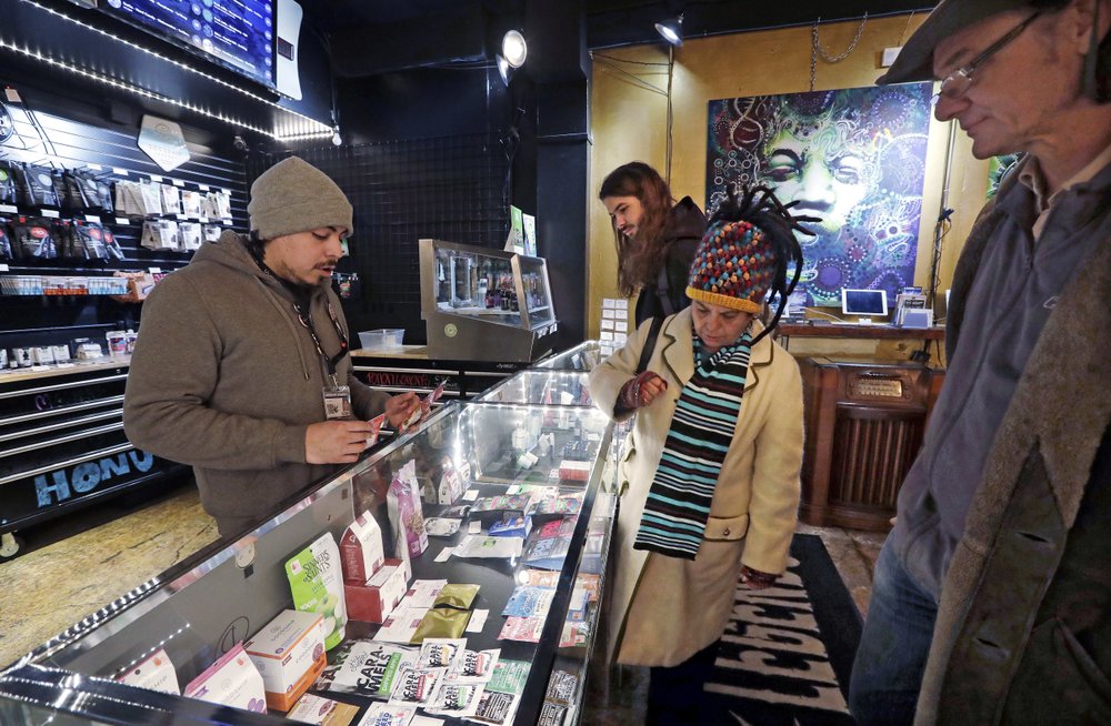 Juan Aguilar, left, assists customers Bill, right, and Nize Nylen and their son Russell shop for edible marijuana products in the Herban Legends pot shop in Seattle. Five years after Washington launched its pioneering legal marijuana market, officials are proposing their most ambitious overhaul yet of the way the industry is regulated, with plans for boosting minority ownership of pot businesses, spreading out oversight among a range of state agencies, and letting the smallest cannabis producers increase the size of the operations in an effort to help them become more competitive. CREDIT: ELAINE THOMPSON/AP