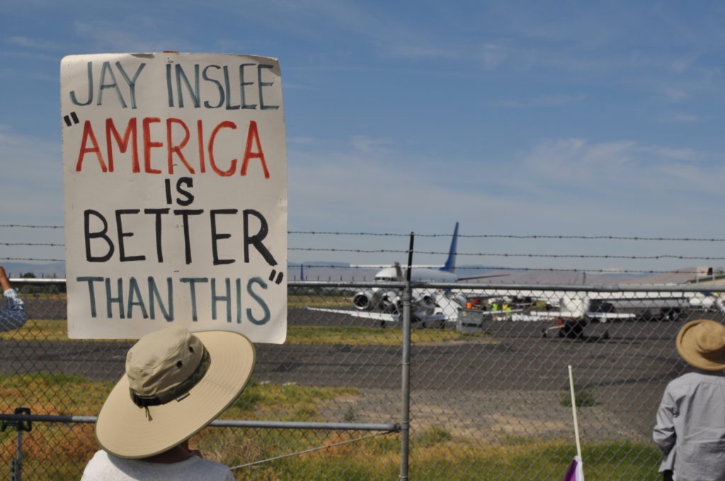 Un activista de la Red de Respuesta a Inmigrantes de Yakima sostiene un cartel que cita al gobernador Jay Inslee mientras 88 detenidos federales detenidos por el Servicio de Inmigración y Control de Aduanas montan un avión el 20 de agosto de 2019. CRÉDITO: ENRIQUE PÉREZ DE LA ROSA / NWPB