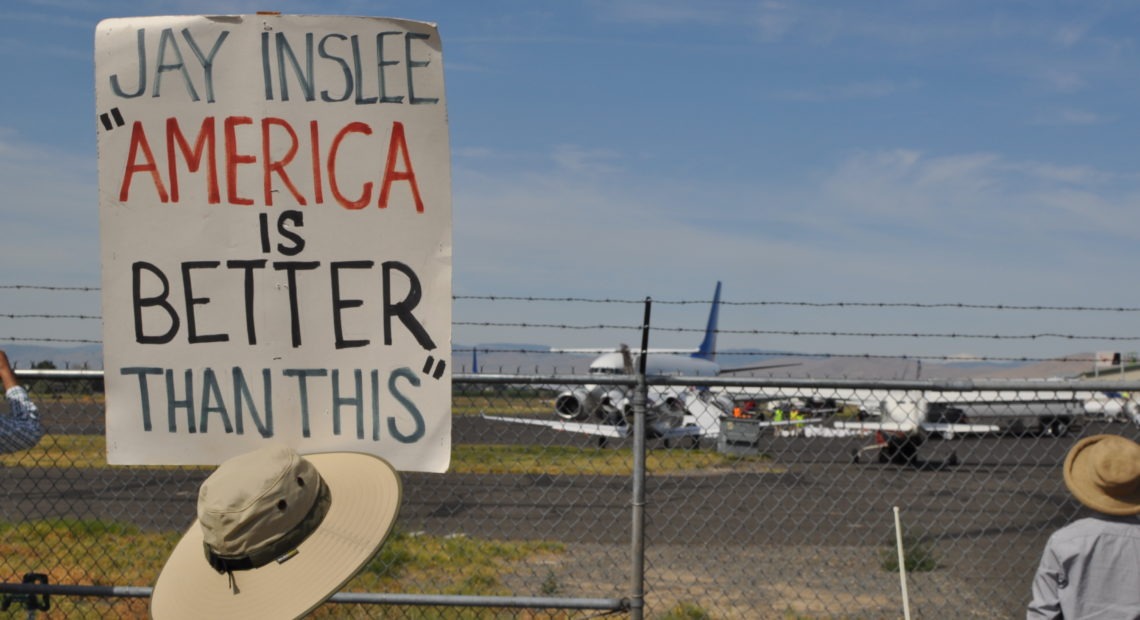 An activist with the Yakima Immigrant Response Network holds a sign quoting Governor Jay Inslee as 88 federal detainees held by Immigration and Customs Enforcement board a plane headed south to El Paso, Texas, likely to be deported. CREDIT: ENRIQUE PÉREZ DE LA ROSA/NWPB