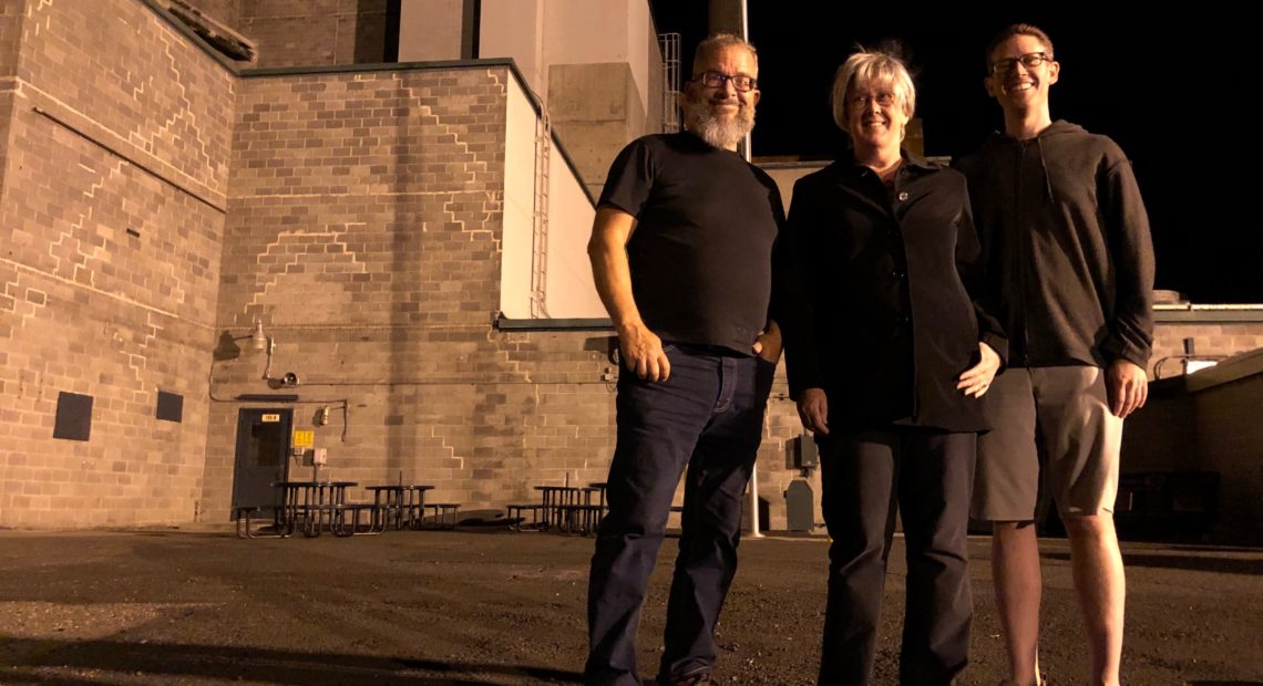 From left, Reg Unterseher, composer, Nancy Welliver, writer, and Mid-Columbia Mastersingers’ artistic director Justin Raffa in front of Hanford’s B Reactor. CREDIT: ANNA KING/N3