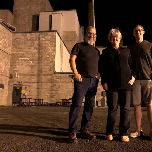 From left, Reg Unterseher, composer, Nancy Welliver, writer, and Mid-Columbia Mastersingers’ artistic director Justin Raffa in front of Hanford’s B Reactor. CREDIT: ANNA KING/N3