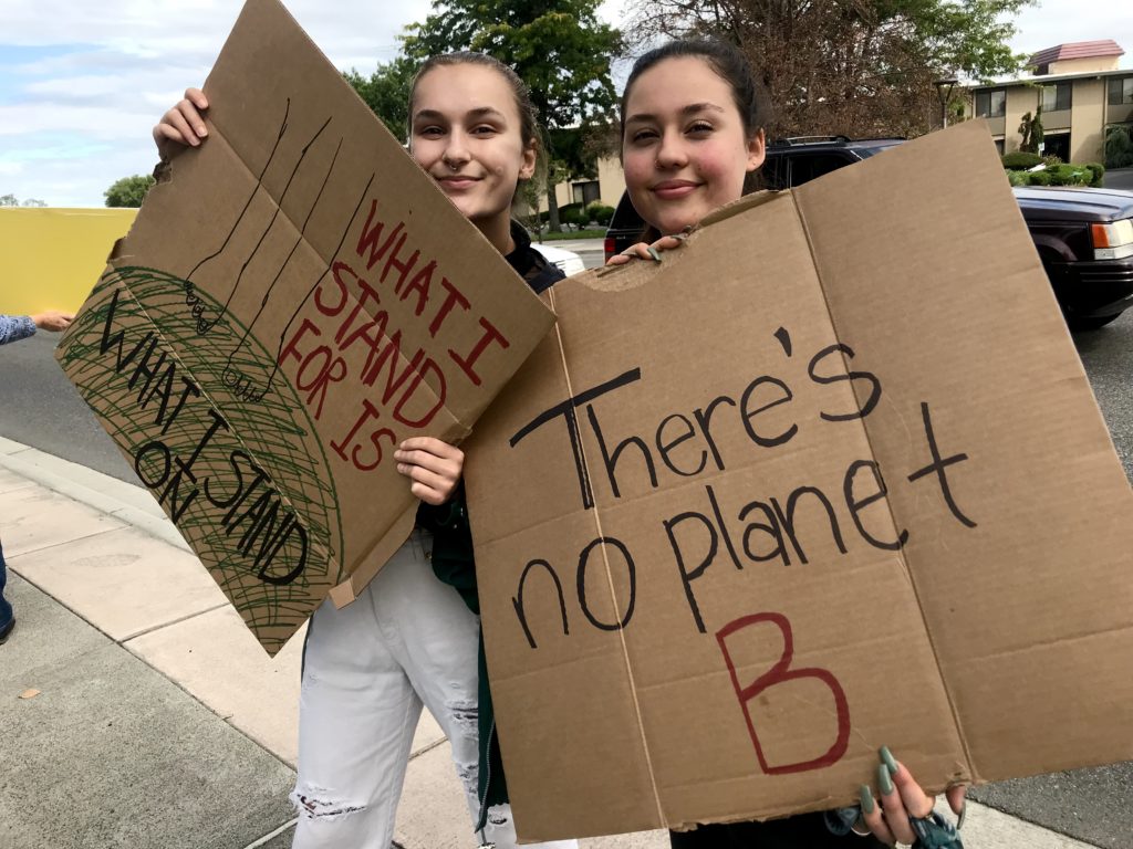 Alexandra Sasha Grieb and Kyleigh Dabler, both 19, from Kennewick, waved at passing cars driving by Richland’s John Dam Plaza. Grieb said it will be up to younger generations to fight climate change now with their votes. “The earth will survive climate change. Humans won’t,” she said. CREDIT: Courtney Flatt/NWPB