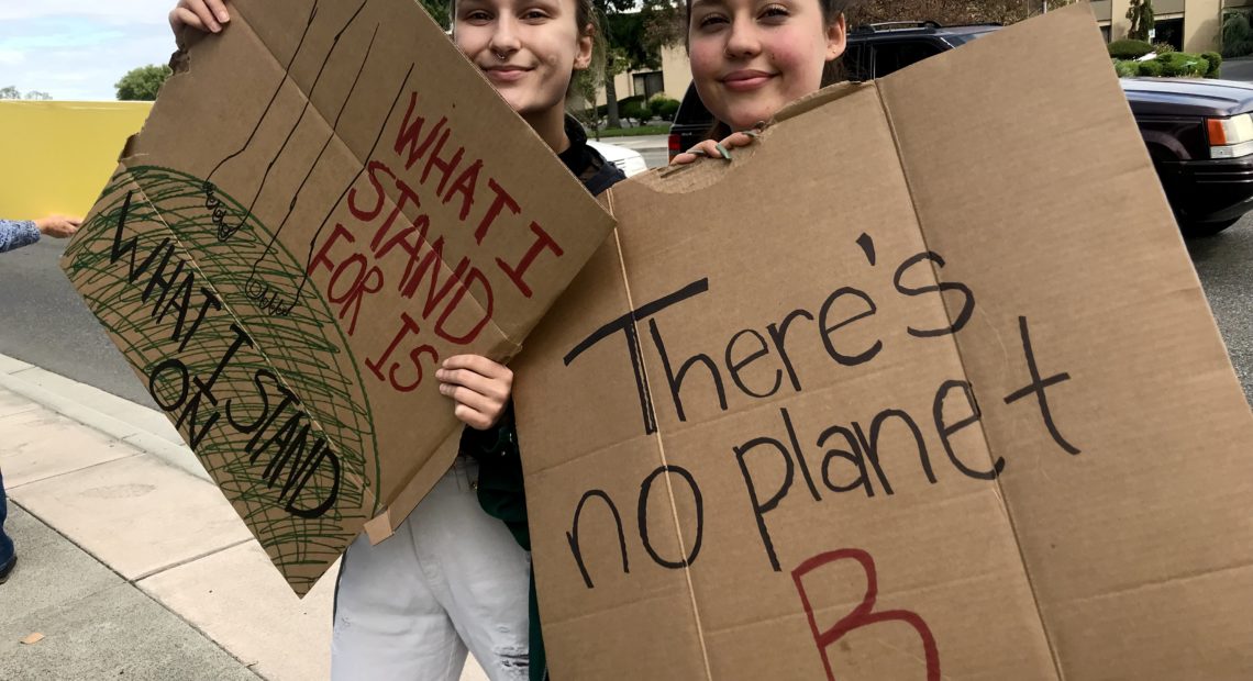 Alexandra Sasha Grieb and Kyleigh Dabler, both 19, from Kennewick, waved at passing cars driving by Richland’s John Dam Plaza. Grieb said it will be up to younger generations to fight climate change now with their votes. “The earth will survive climate change. Humans won’t,” she said. CREDIT: Courtney Flatt/NWPB