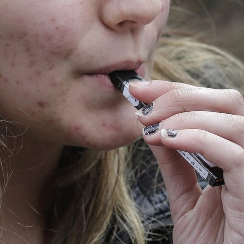 In this April 11, 2018 file photo, a high school student uses a vaping device near a school campus in Cambridge, Mass. CREDIT: STEVEN SENNE/AP