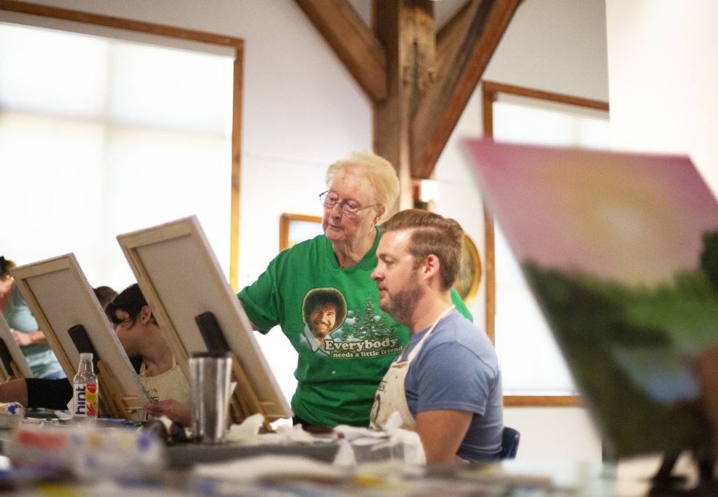 Sandra Hill offers guidance to Mark Scheiffley during a Bob Ross painting class at the Franklin Parks Art Center in Purcellville, Va., on Sept. 20. Hill is one of more than 3,000 people certified to teach the Bob Ross wet-on-wet painting technique. CREDIT: Mhari Shaw/NPR